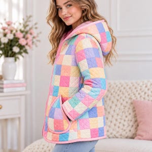 Peut inclure: Une veste matelass&eacute;e pr&eacute;sentant un motif &agrave; damier pastel multicolore dans des tons de rose, bleu, jaune et lavande. La veste comprend une capuche, des manches longues et deux grandes poches plaqu&eacute;es arrondies, le tout bord&eacute; d'un liser&eacute; rose.