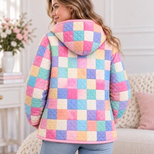 Peut inclure: Une veste matelass&eacute;e avec un motif &agrave; carreaux multicolores dans des tons de rose, bleu, jaune et orange. La veste comprend une capuche et des manches longues, avec un liser&eacute; rose uni sur les bords et une texture piqu&eacute;e en losanges.