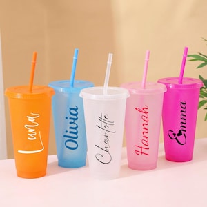 May include: Five translucent plastic tumblers with matching lids and straws, each featuring a unique name in black or white script lettering. The cups are coloured orange, blue, clear, light pink, and dark pink, arranged in a row.