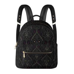 Puede incluir: Una mochila negra con un patrón oscuro e intrincado estilo damasco, con sutiles acentos morados y ojos amarillos brillantes integrados en el diseño. La bolsa incluye correas negras, un asa superior y un bolsillo frontal con cremallera dorada.