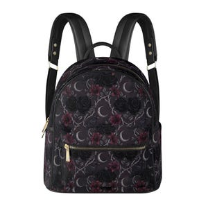 Könnte beinhalten: Ein schwarzer Rucksack mit einem sich wiederholenden Muster aus dunklen Rosen, tiefroten Lilien, Mondsicheln und kleinen Vögeln auf dornigen Ranken. Die Tasche verfügt über eine vordere Reißverschlusstasche mit goldfarbenen Beschlägen und verstellbare Träger.