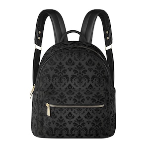 May include: A black backpack featuring a dark grey damask pattern across the main body and front pocket. The bag includes black shoulder straps, a top handle, and gold-toned metal zips on the main compartment and the front exterior pocket.