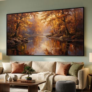 May include: A large rectangular landscape painting featuring a dense forest with vibrant orange and golden autumn foliage reflected in a calm river. The artwork is framed in black and depicts a serene woodland scene with warm light filtering through trees.