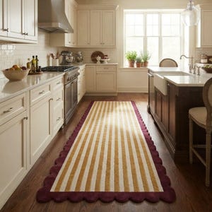 Puede incluir: Una alfombra de pasillo rectangular larga con rayas verticales en color amarillo mostaza y crema. La alfombra presenta un borde festoneado en un tono burdeos intenso, creando un contorno definido que contrasta con el diseño central.