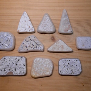 May include: A collection of 11 white and gray speckled ceramic tiles in various shapes, including triangles, squares, and irregular shapes.