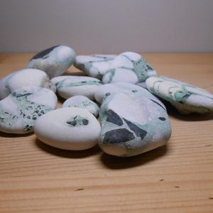 Könnte beinhalten: Eine Sammlung glatter, weißer Steine mit grüner und schwarzer Marmorierung. Die Steine liegen auf einer Holzoberfläche.