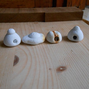 Può includere: Quattro prese da arrampicata in ceramica bianca con forme diverse e un piccolo foro al centro. Le prese sono disposte in fila su una superficie di legno marrone chiaro.