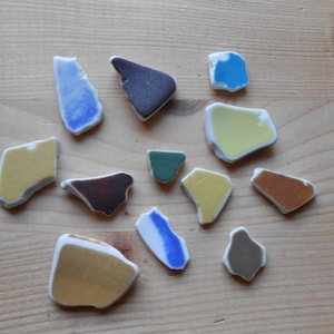 Può includere: Assortimento di piastrelle in ceramica colorate in varie forme e dimensioni. Le piastrelle sono in tonalità di blu, verde, giallo, marrone e grigio.