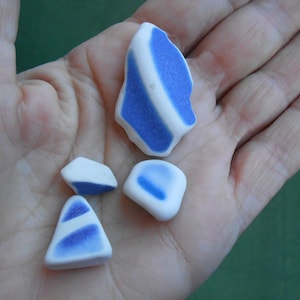 May include: Four pieces of sea glass with a white background and blue swirls. The sea glass is smooth and has been tumbled by the ocean.