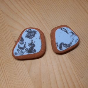 Può includere: Due pietre lisce e arrotondate di colore terracotta con uno sfondo bianco e un motivo a marmo nero.