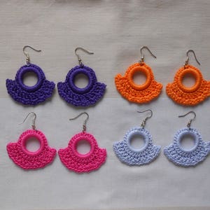 Könnte beinhalten: Sechs Paare gehäkelter Ohrringe in verschiedenen Farben, darunter Lila, Orange, Pink und Hellblau. Jedes Paar hat ein kreisförmiges Design mit einem gewellten Rand.