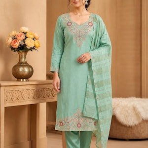 May include: A light mint green long-sleeved tunic and matching trousers set featuring intricate red and gold embroidery around the neckline and hem, paired with a coordinating sheer mint green dupatta with horizontal gold stripes.