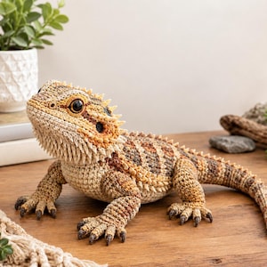 Op de afbeelding: Een gehaakt baardagaam knuffeldier met een textuurrijk lichaam van beige, bruin en oranje garen. De hagedis heeft een stekelige baard, donkerbruine ogen en gedetailleerde klauwen aan elke poot, gemaakt met ingewikkelde steken.