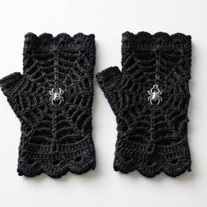 May include: A pair of black fingerless gloves featuring a crocheted spiderweb pattern. Each glove is adorned with a small, metallic silver spider charm centered on the web design. The edges of the gloves have a scalloped, decorative crochet trim.