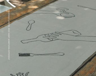 Puede incluir: Un camino de mesa gris claro con ilustraciones bordadas en negro de utensilios de comedor, una botella de vino y un sacacorchos. El texto FOR DESIGN LOVERS, WHO WANT SOMETHING DIFFERENT y la marca MŌOBI están impresos en la tela.