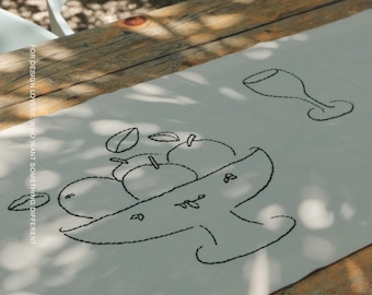 Puede incluir: Un camino de mesa blanco con bordados de líneas negras que representan un frutero y una copa de vino. El texto FOR DESIGN LOVERS, WHO WANT SOMETHING DIFFERENT está impreso verticalmente y la marca MŌOBI en la esquina inferior.