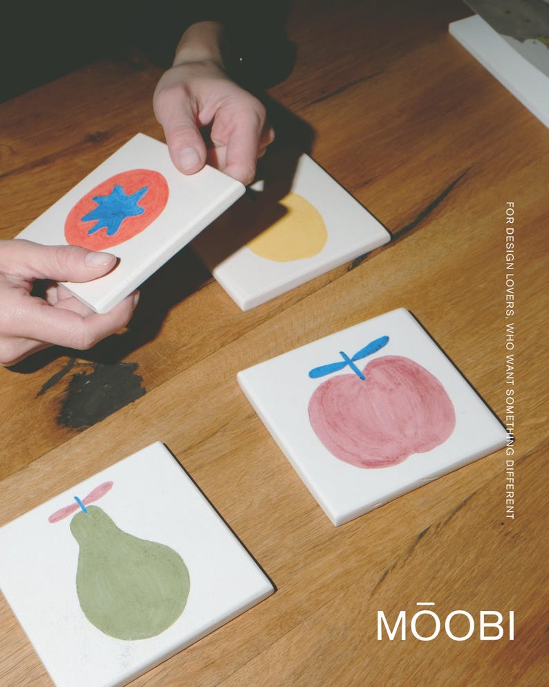 Puede incluir: Cuatro azulejos cuadrados de cer&aacute;mica blanca con ilustraciones de frutas pintadas a mano, incluyendo un tomate rojo con una estrella azul, un c&iacute;rculo amarillo, una manzana rosa con tallo azul y una pera verde con tallo rosa. Texto: FOR DESIGN LOVERS, WHO WANT SOMETHING DIFFERENT y MŌOBI.