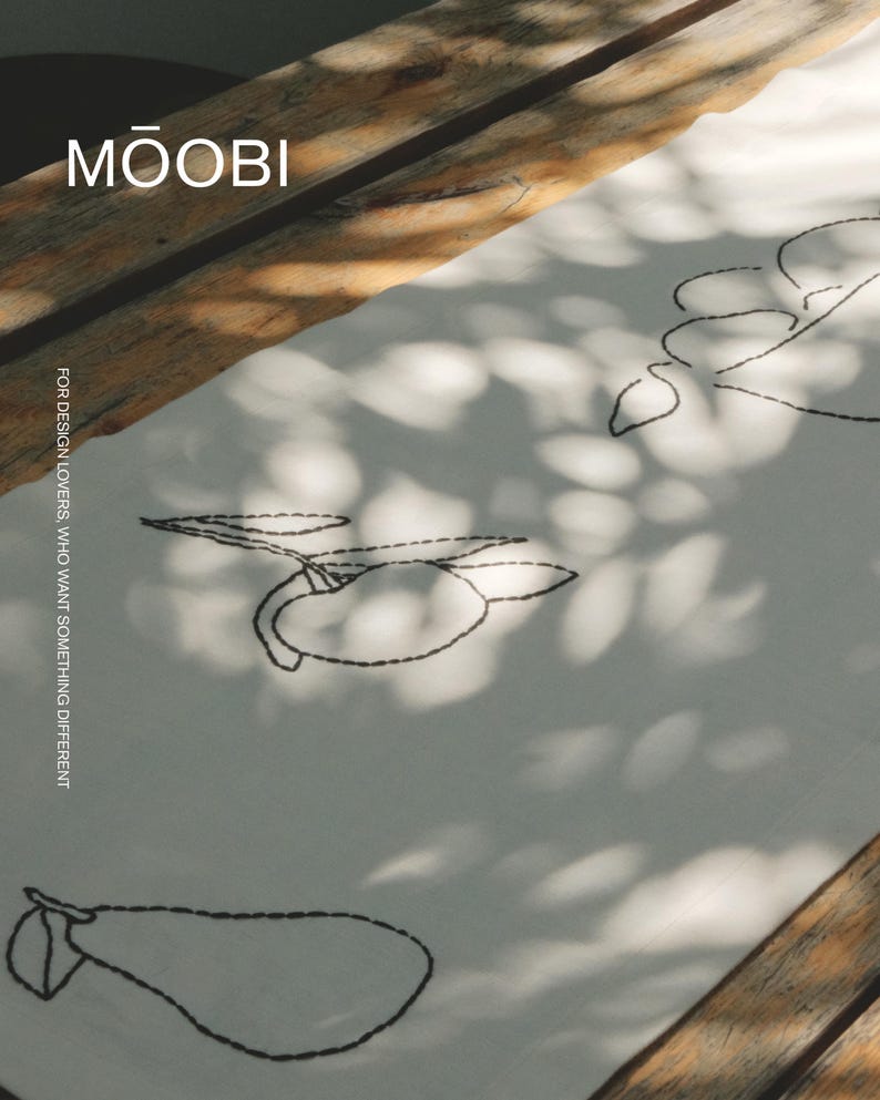 Pu&ograve; includere: Un runner da tavola in tessuto bianco con ricami neri che raffigurano disegni al tratto di vari frutti, tra cui pere e limoni. Il testo MŌOBI e FOR DESIGN LOVERS, WHO WANT SOMETHING DIFFERENT &egrave; stampato nell'angolo in alto a sinistra.