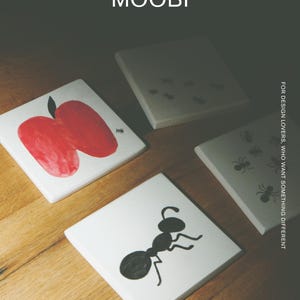 Pu&ograve; includere: Quattro sottobicchieri quadrati bianchi con illustrazioni grafiche nere e rosse di formiche e una mela. Il testo MŌOBI &egrave; in alto e il testo FOR DESIGN LOVERS, WHO WANT SOMETHING DIFFERENT &egrave; stampato verticalmente sul lato destro.