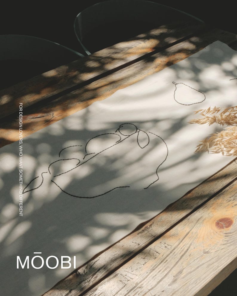 Pu&ograve; includere: Un runner da tavola in tessuto color crema con ricami a linee nere che raffigurano una pera e un gruppo di frutti. Il testo "FOR DESIGN LOVERS, WHO WANT SOMETHING DIFFERENT" e "MŌOBI" &egrave; stampato sul tessuto con un carattere sans-serif.
