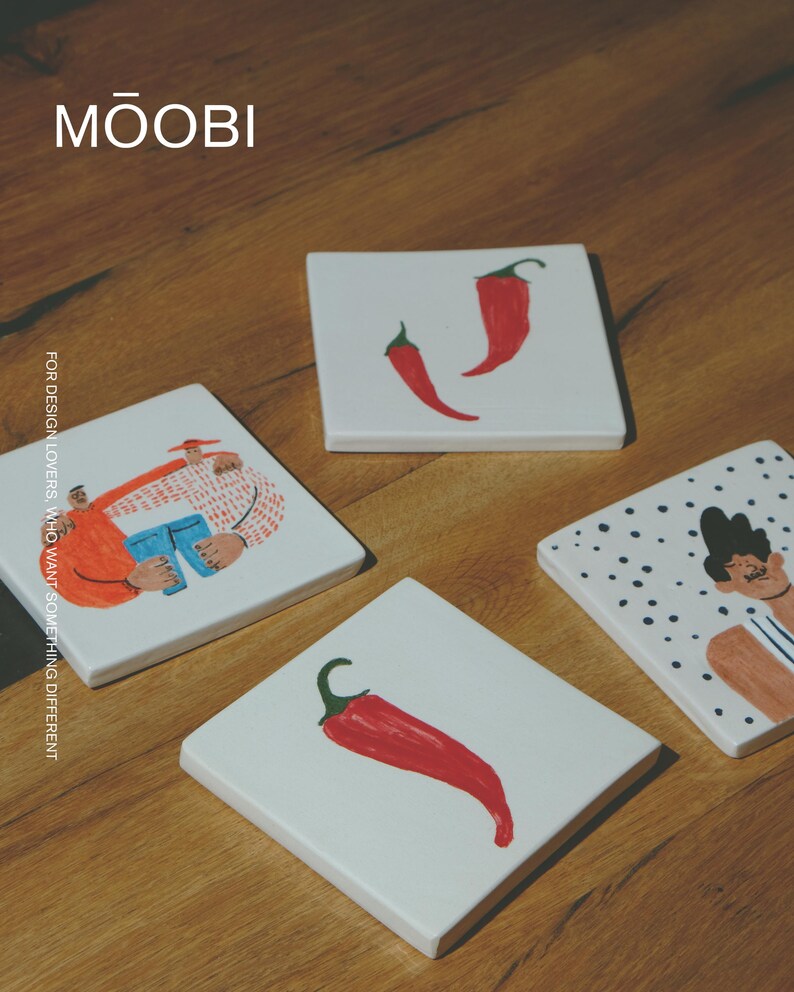May include: Four square white ceramic coasters featuring hand-painted illustrations. One shows two figures embracing, one features a single red chili pepper, one displays two red chili peppers, and one depicts a person against a black polka dot background.