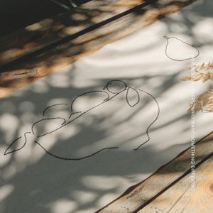 Pu&ograve; includere: Un runner in tessuto color crema con ricamo a linee nere raffigurante una pera e un ramo con foglie. Il testo MŌOBI &egrave; stampato nell'angolo in alto a destra, con il testo FOR DESIGN LOVERS WHO WANT SOMETHING DIFFERENT disposto verticalmente.