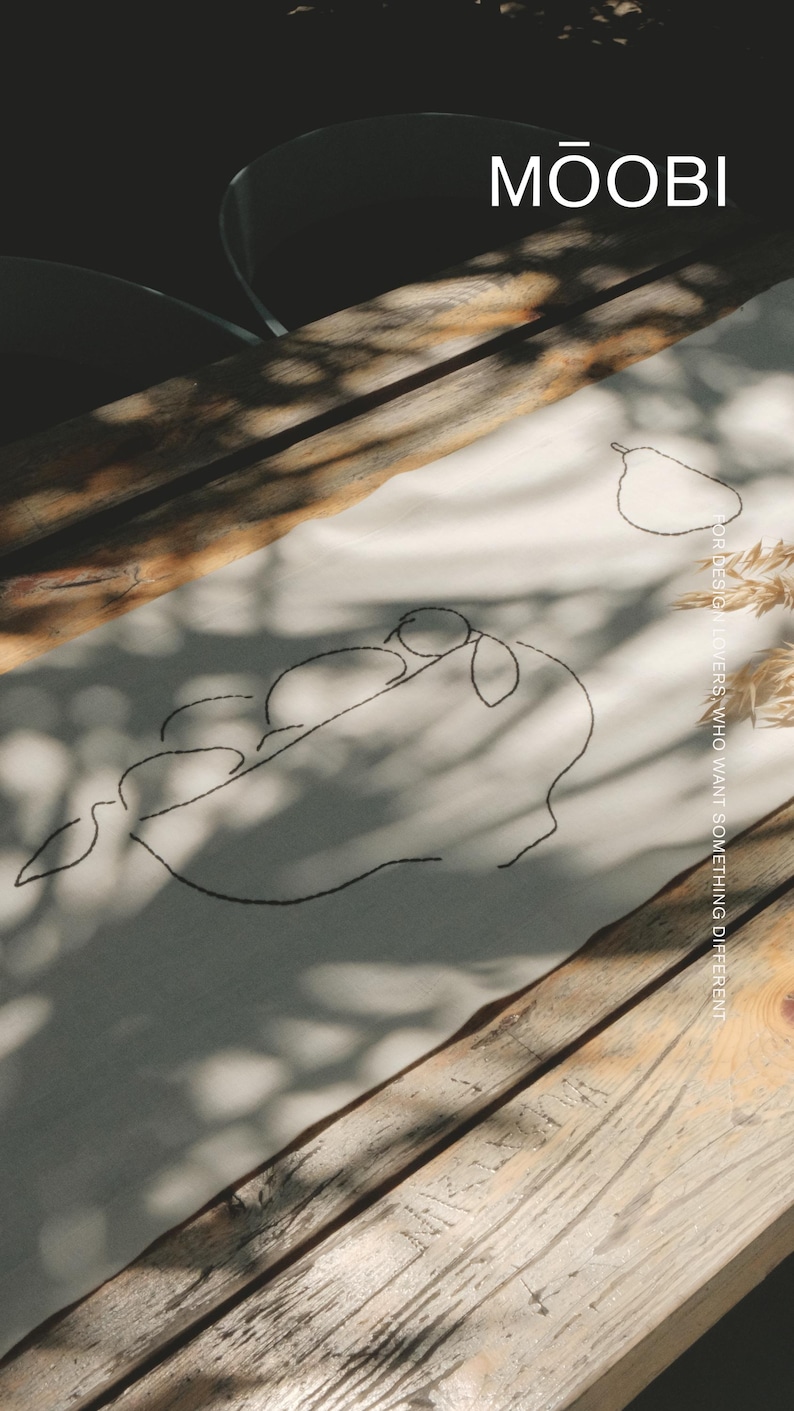 Pu&ograve; includere: Un runner in tessuto color crema con ricamo a linee nere raffigurante una pera e un ramo con foglie. Il testo MŌOBI &egrave; stampato nell'angolo in alto a destra, con il testo FOR DESIGN LOVERS WHO WANT SOMETHING DIFFERENT disposto verticalmente.