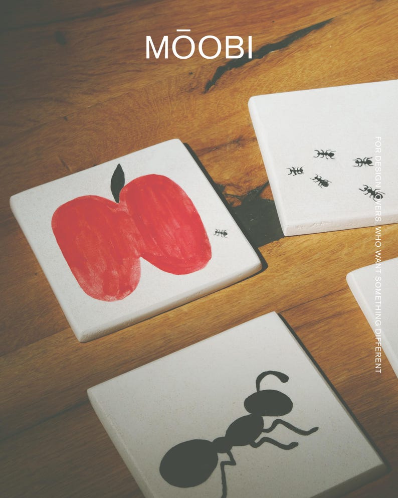 Pu&ograve; includere: Tre sottobicchieri quadrati bianchi con illustrazioni grafiche nere e rosse. Un sottobicchiere mostra una mela rossa con una piccola formica nera, un altro cinque piccole formiche nere e il terzo una grande formica nera. &Egrave; visibile il testo MŌOBI.