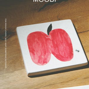 Pu&ograve; includere: Un sottobicchiere quadrato bianco con un'illustrazione di una mela rossa in stile disegno a mano, un picciolo nero e una piccola grafica di una formica nera. Il testo MŌOBI e FOR DESIGN LOVERS, WHO WANT SOMETHING DIFFERENT &egrave; stampato sopra.