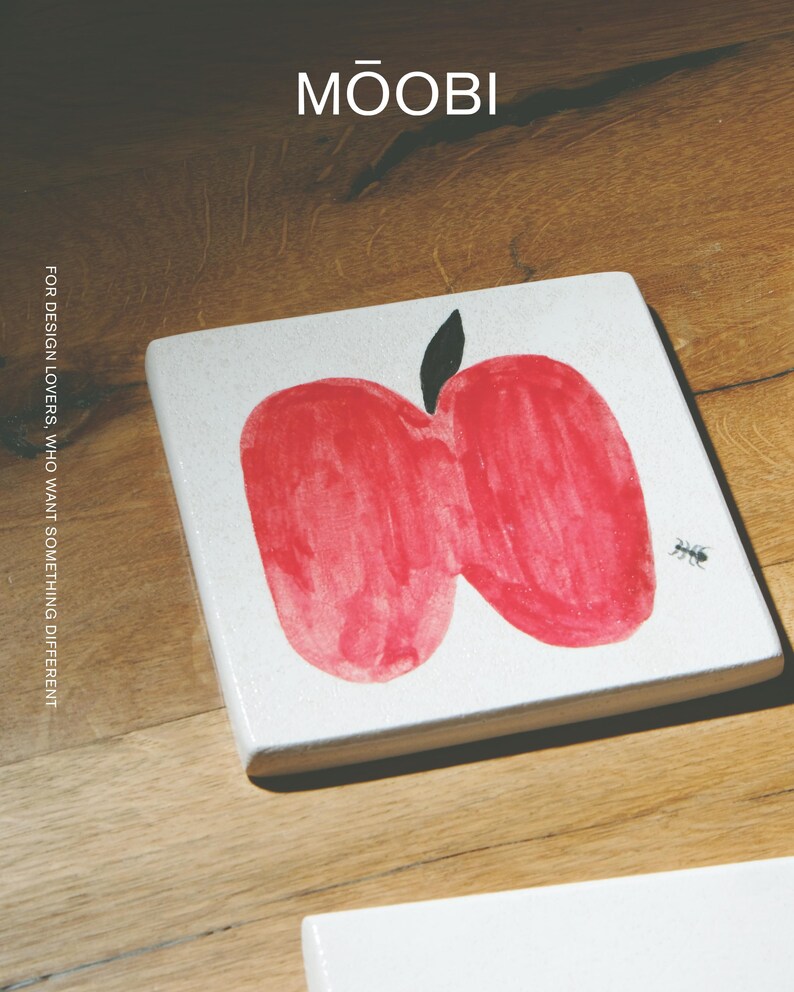 Pu&ograve; includere: Un sottobicchiere quadrato bianco con un'illustrazione di una mela rossa in stile disegno a mano, un picciolo nero e una piccola grafica di una formica nera. Il testo MŌOBI e FOR DESIGN LOVERS, WHO WANT SOMETHING DIFFERENT &egrave; stampato sopra.