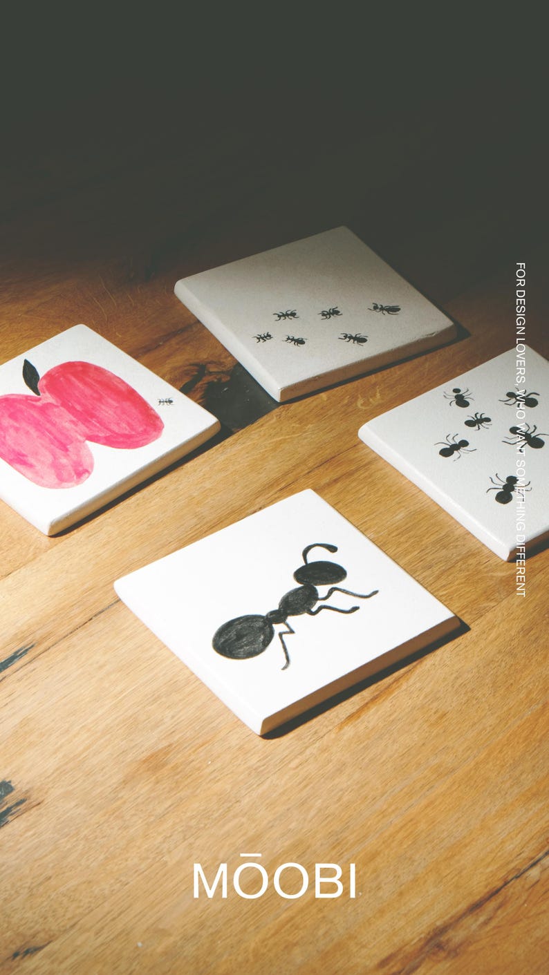 Pu&ograve; includere: Quattro sottobicchieri quadrati in ceramica bianca con illustrazioni a inchiostro nero di formiche e una mela rosa. Un sottobicchiere mostra una grande formica, un altro diverse piccole formiche e uno una mela rosa. Testo: MOOBI e FOR DESIGN LOVERS, WHO WANT SOMETHING DIFFERENT.