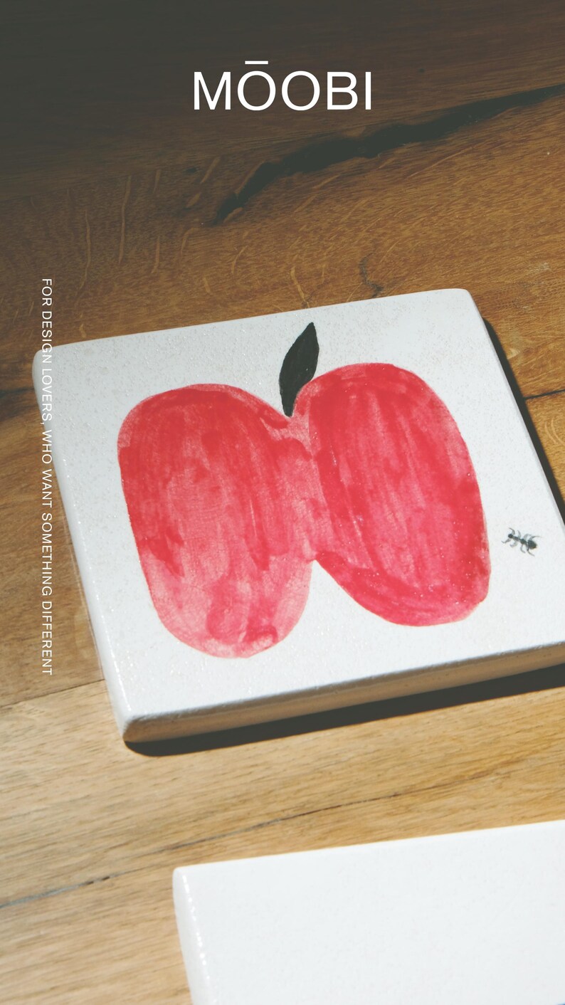 Pu&ograve; includere: Una piastrella quadrata bianca con un'illustrazione di una mela rossa disegnata a mano con un picciolo nero e una piccola formica nera. Il testo MŌOBI &egrave; stampato in alto e FOR DESIGN LOVERS, WHO WANT SOMETHING DIFFERENT sul lato sinistro.
