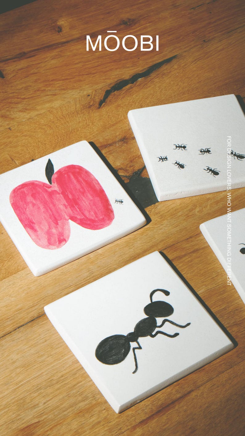 Pu&ograve; includere: Tre sottobicchieri quadrati in ceramica bianca con illustrazioni a inchiostro nero e rosso. Un sottobicchiere mostra una grande mela rossa con una minuscola formica nera, un altro una singola grande formica nera e il terzo presenta diverse piccole formiche nere.