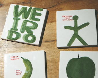 Puede incluir: Cuatro azulejos de cerámica blancos cuadrados con ilustraciones y texto en verde pintados a mano. Un azulejo dice WEIRDO, otro muestra una figura de palo con REGISTER YOUR EXISTENCE, uno muestra un plátano con GREEN BANANA YOU MUST WAIT YOU MUST BE PATIENT, y otro una manzana con WATCH IT ROT.