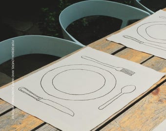 Puede incluir: Manteles individuales rectangulares de color blanco roto con un contorno bordado en negro de un plato, tenedor, cuchillo y cuchara. El texto MŌOBI y FOR DESIGN LOVERS, WHO WANT SOMETHING DIFFERENT aparece en la imagen sobre una mesa de madera.