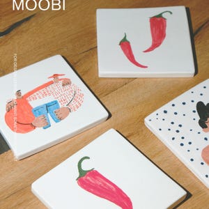 May include: Four square white ceramic coasters featuring hand-painted illustrations. One shows two figures, another has a single red chili pepper, a third displays two red chili peppers, and the fourth features a person with blue polka dots.