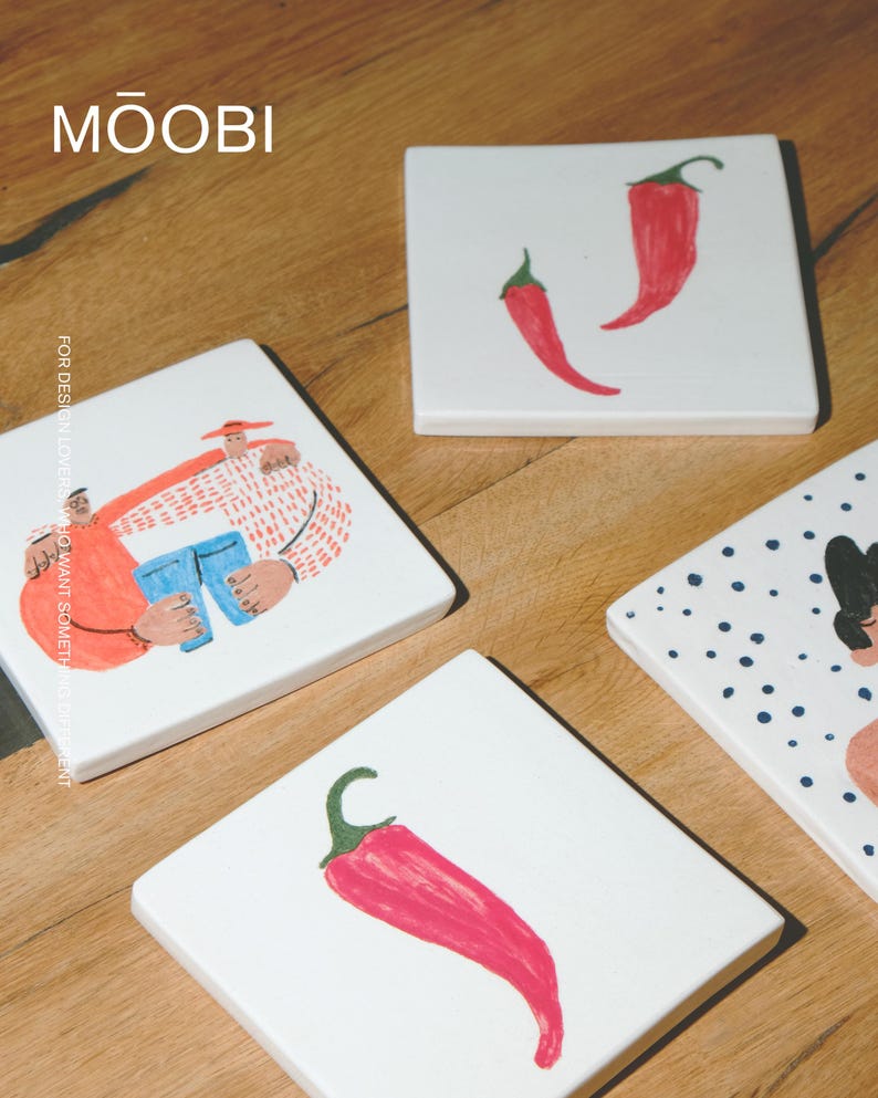 May include: Four square white ceramic coasters featuring hand-painted illustrations. One shows two figures, another has a single red chili pepper, a third displays two red chili peppers, and the fourth features a person with blue polka dots.