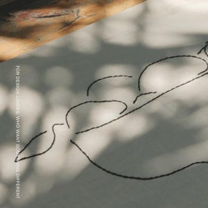 Pu&ograve; includere: Un tessuto di colore chiaro con un disegno a linee ricamate in nero che raffigura tre forme arrotondate. Il testo "FOR DESIGN LOVERS, WHO WANT SOMETHING DIFFERENT" &egrave; stampato verticalmente e il marchio "MŌOBI" appare in basso.