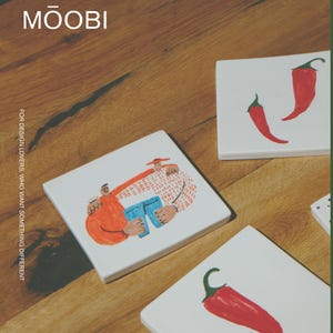 May include: Three square white ceramic coasters. One coaster features a colorful illustration of two figures embracing, while the other two coasters each display a single red chili pepper. The text MŌOBI and FOR DESIGN LOVERS, WHO WANT SOMETHING DIFFERENT is visible.