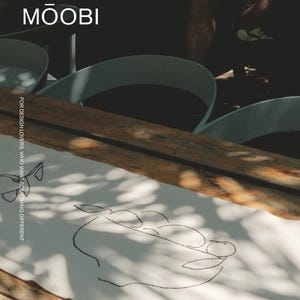 Pu&ograve; includere: Un runner da tavola in tessuto bianco con un disegno ricamato a filo nero che raffigura una ciotola con frutta. Il testo MŌOBI &egrave; stampato in alto e il testo FOR DESIGN LOVERS, WHO WANT SOMETHING DIFFERENT &egrave; stampato verticalmente sul lato.