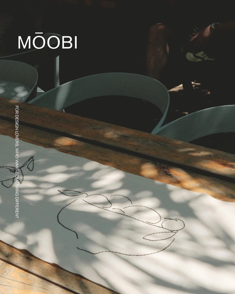 Pu&ograve; includere: Un runner da tavola in tessuto bianco con un disegno ricamato a filo nero che raffigura una ciotola con frutta. Il testo MŌOBI &egrave; stampato in alto e il testo FOR DESIGN LOVERS, WHO WANT SOMETHING DIFFERENT &egrave; stampato verticalmente sul lato.