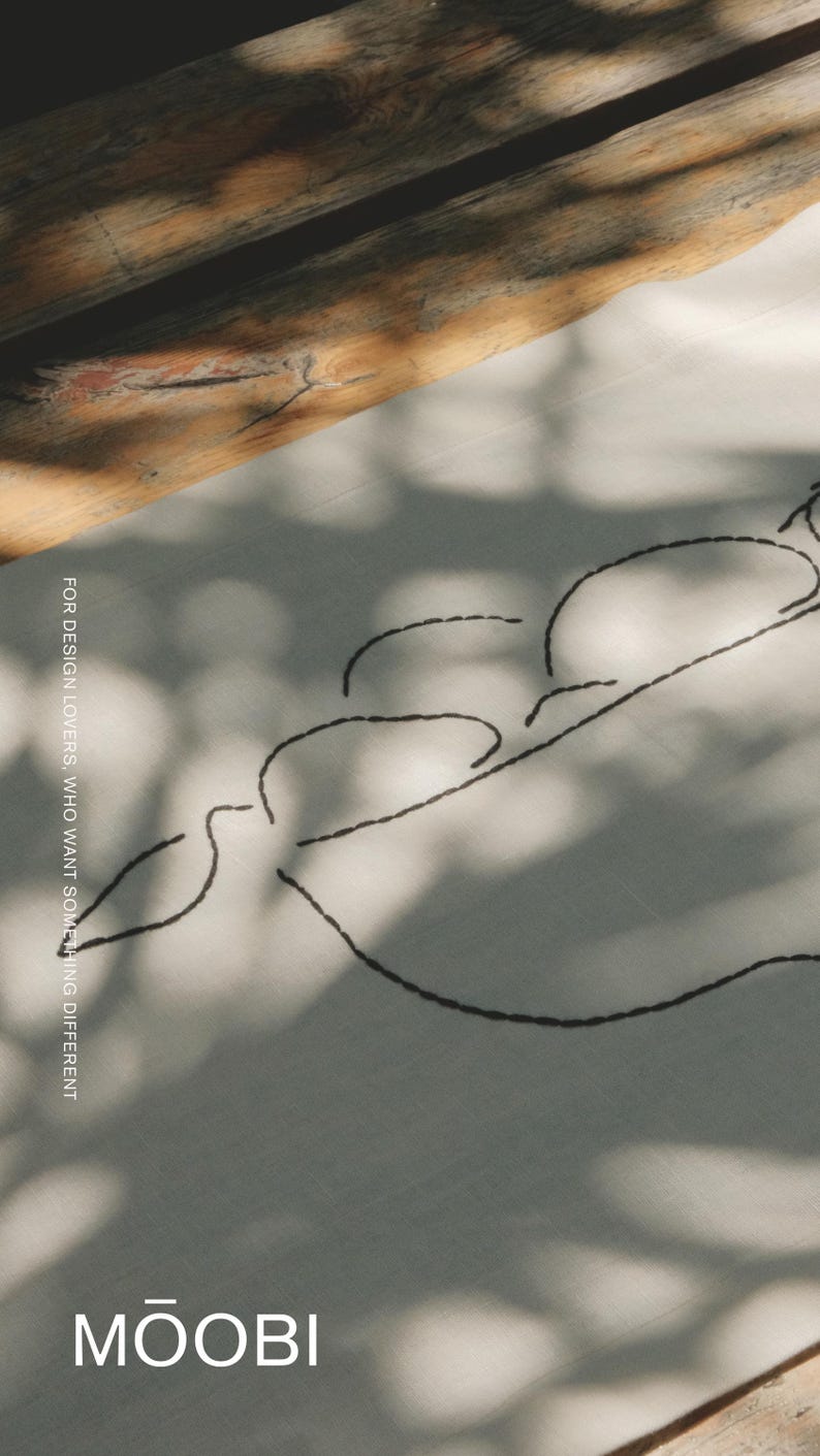 Pu&ograve; includere: Un tessuto di colore chiaro con un disegno a linee ricamate in nero che raffigura tre forme arrotondate. Il testo "FOR DESIGN LOVERS, WHO WANT SOMETHING DIFFERENT" &egrave; stampato verticalmente e il marchio "MŌOBI" appare in basso.