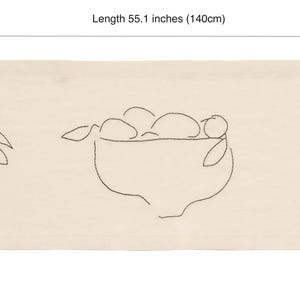 Pu&ograve; includere: Un runner da tavola rettangolare color bianco sporco con un'illustrazione a linee nere di una ciotola di frutta e frutti singoli. Il runner misura 140 cm di lunghezza e 40 cm di larghezza, mostrando pere e agrumi con foglie sui gambi.