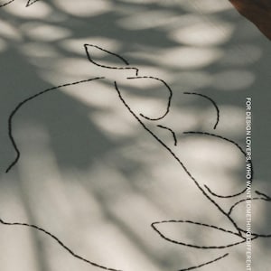 Pu&ograve; includere: Un tessuto bianco con ricami neri che raffigurano disegni botanici a linee. Il tessuto riporta il testo "FOR DESIGN LOVERS, WHO WANT SOMETHING DIFFERENT" e il nome del marchio "MOOBI" stampato in bianco nell'angolo in basso a destra.