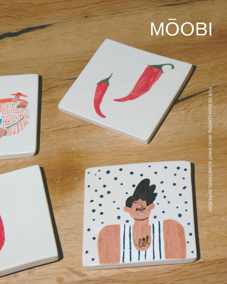 May include: Three square white ceramic tiles featuring hand-painted illustrations. One tile displays two red chili peppers, another shows a person in a striped tank top against blue dots, and the third shows a person in a hat. Text reads MŌOBI.