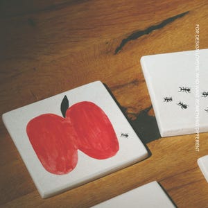 Pu&ograve; includere: Tre sottobicchieri quadrati bianchi con illustrazioni grafiche nere e rosse. Uno mostra una mela rossa con una piccola formica nera, un altro una grande formica nera e il terzo tre piccole formiche con il testo FOR DESIGN LOVERS, WHO WANT SOMETHING DIFFERENT. Il marchio MŌOBI &egrave; stampato in alto.