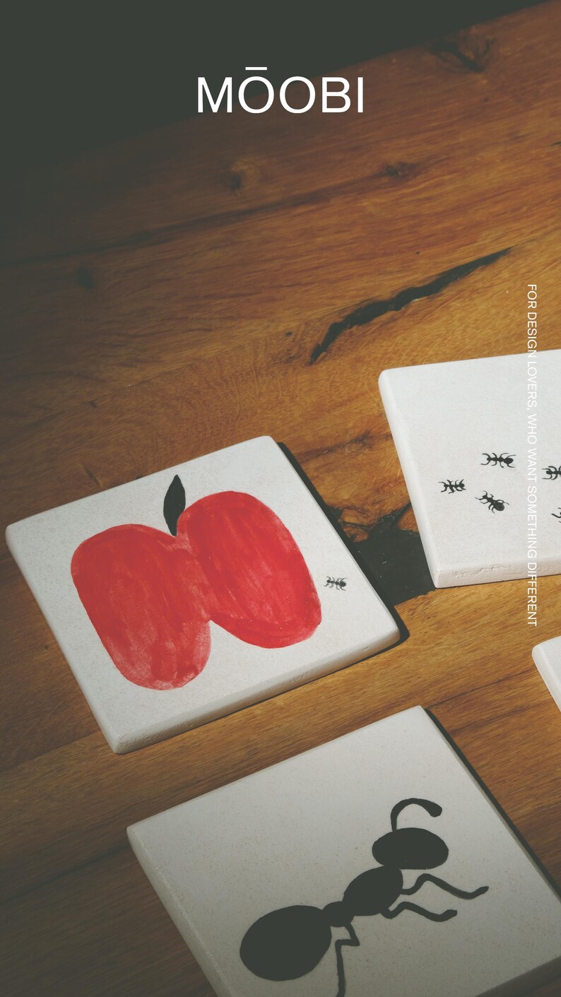 Pu&ograve; includere: Tre sottobicchieri quadrati bianchi con illustrazioni grafiche nere e rosse. Uno mostra una mela rossa con una piccola formica nera, un altro una grande formica nera e il terzo tre piccole formiche con il testo FOR DESIGN LOVERS, WHO WANT SOMETHING DIFFERENT. Il marchio MŌOBI &egrave; stampato in alto.