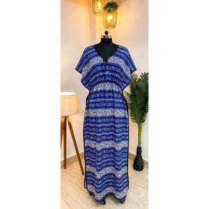 May include: A floor-length kaftan dress featuring a vibrant blue and white horizontal pattern with intricate swirling designs. The garment has short, wide sleeves, a V-neckline with a small black tie detail, and a cinched waistline.