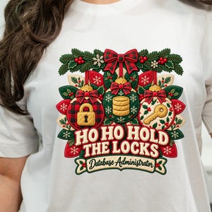 Può includere: Una t-shirt bianca con una grafica festiva composta da tre decorazioni natalizie raffiguranti un lucchetto, una pila di monete e una chiave. Il design include fiocchi a quadri rossi, agrifoglio e fiocchi di neve, con il testo HO HO HOLD THE LOCKS Database Administrator.