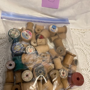 May include: A clear plastic bag filled with vintage wooden spools of thread. The spools are various sizes and shapes, with some featuring colorful paper labels. A purple sticky note with the number 5 is in the background.